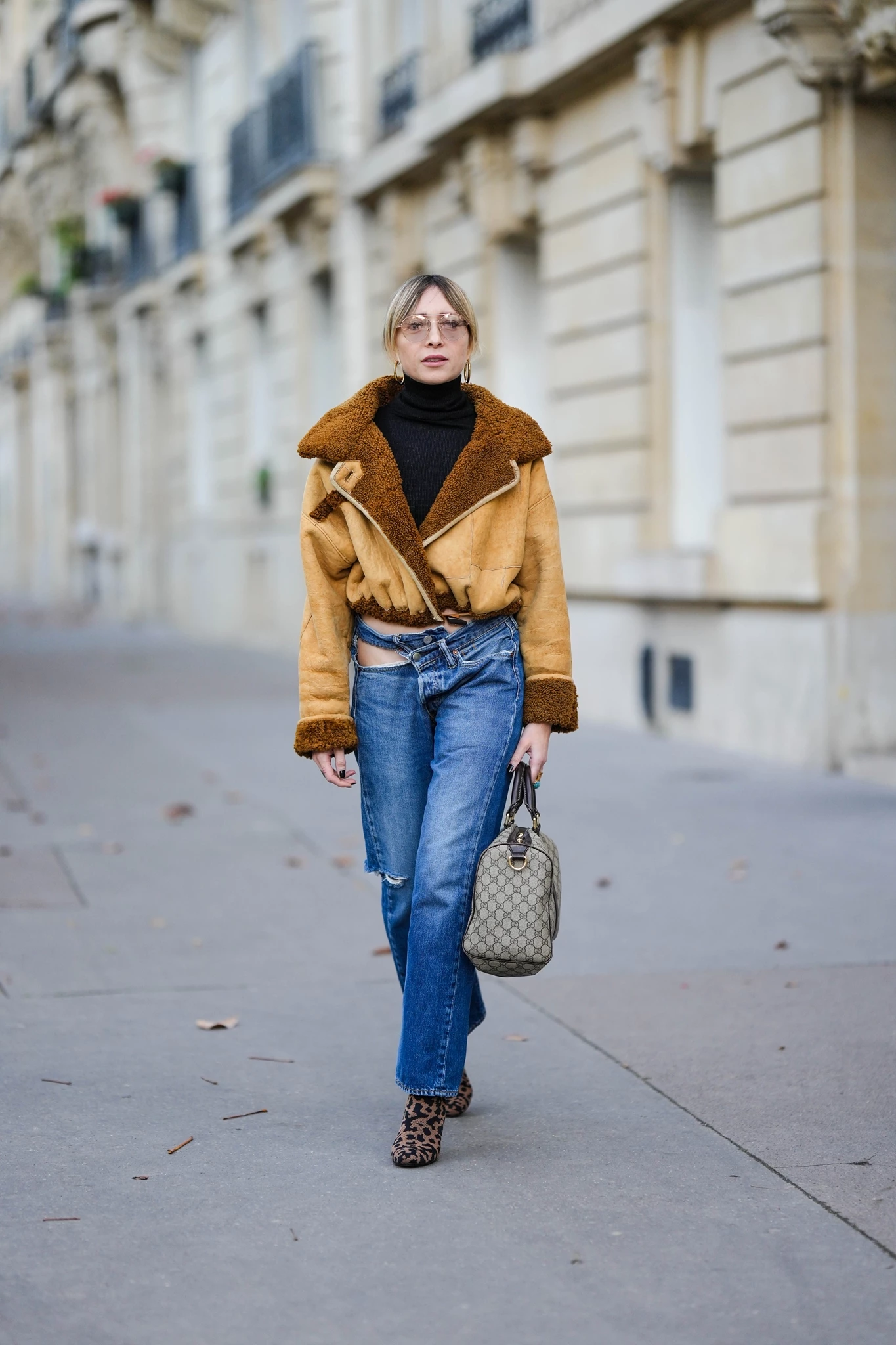 Γυναίκα που φοράει τζιν παντελόνι με shearling τζάκετ και μποτάκια με λεοπάρ μοτίβο, ενώ κρατάει μεγάλη τσάντα.