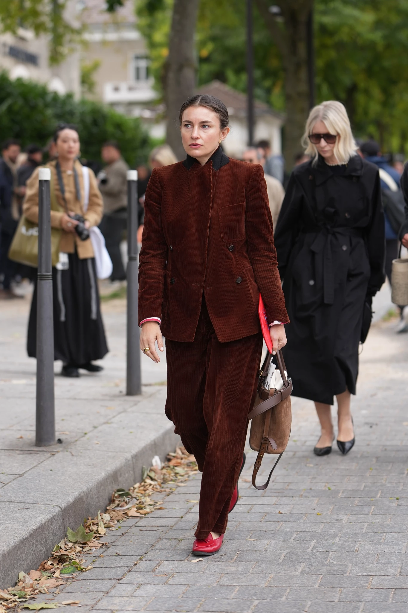 Γυναίκα περπατά στον δρόμο φορώντας ένα  κοστούμι από καφέ κοτλέ ύφασμα (σακάκι και παντελόνι) και κόκκινα μοκασίνια. Κρατάει μια δερμάτινη τσάντα.