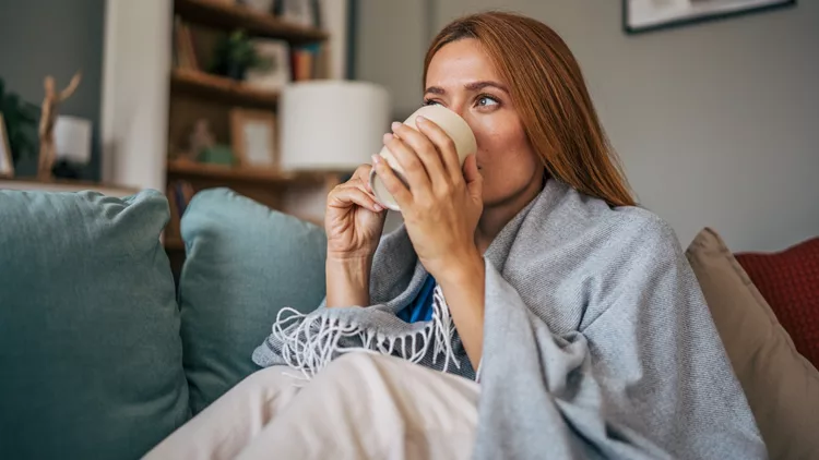 Sick woman drinking hot beverage on sofa at home