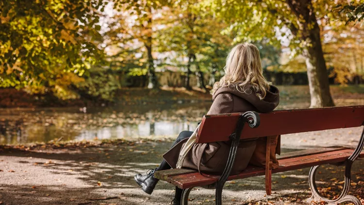 Woman in coat resting and sitting on bench in autumn park