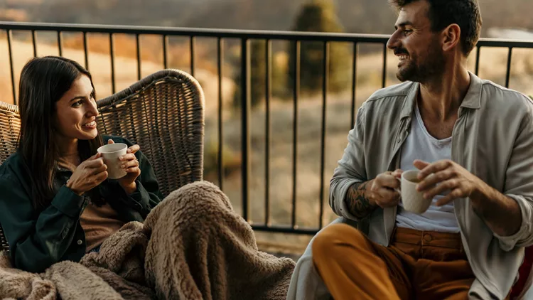 Young couple relaxing on balcony, enjoying coffee and scenic view