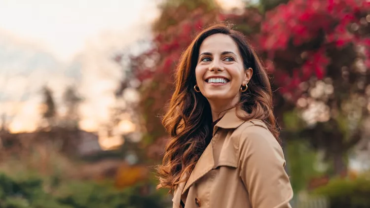 Happy woman smiling and looking away in autumn park during sunset