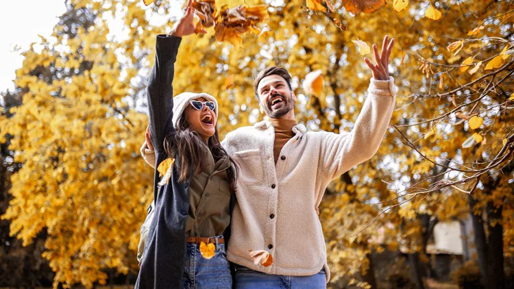 Smiling young couple walking in autumn park, holding colorful leaf together and enjoying romantic fall day