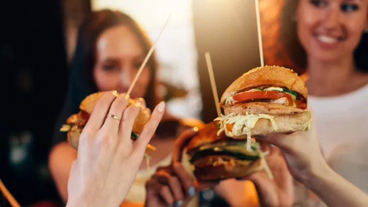 Female hands holding big tasty juicy hamburgers with blurred women in background