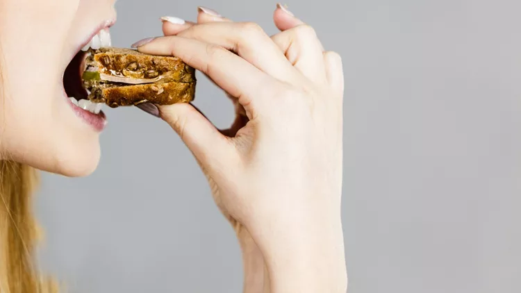 Woman eating sandwich, taking bite