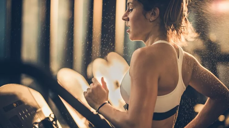 Sweaty woman running on treadmill during sports training in a gym.