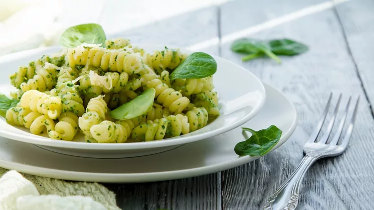 delicious pasta dish with creamy spinach sauce decorated with spinach leaves on grey wooden background