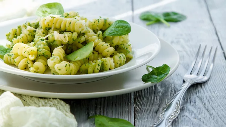 delicious pasta dish with creamy spinach sauce decorated with spinach leaves on grey wooden background