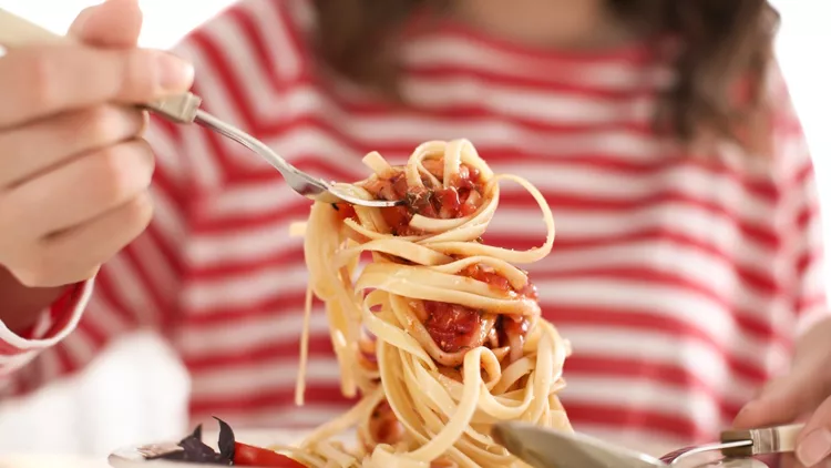 Young woman eating tasty pasta at table, closeup
