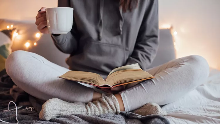 Girl drinking hot tea and reading book in bed