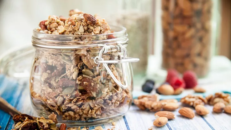 A glass jar in a blue wooden table overfilled with granola