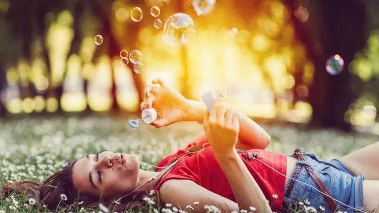 relaxed-woman-blowing-soap-bubbles-in-the-park-picture-id700171470