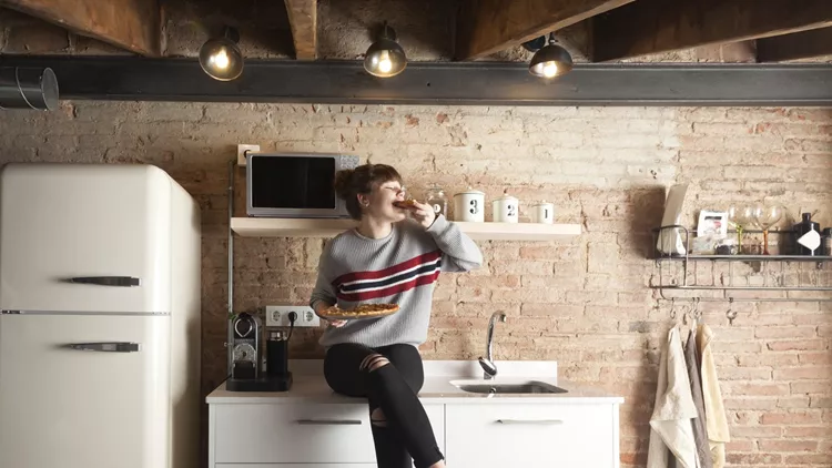 Beautiful girl eating pizza in a modern kitchen