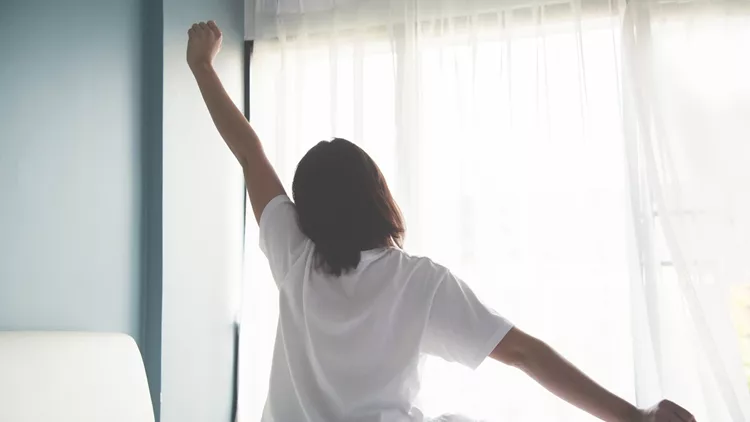 Asian woman waking up in the morning. Outstretched arms.