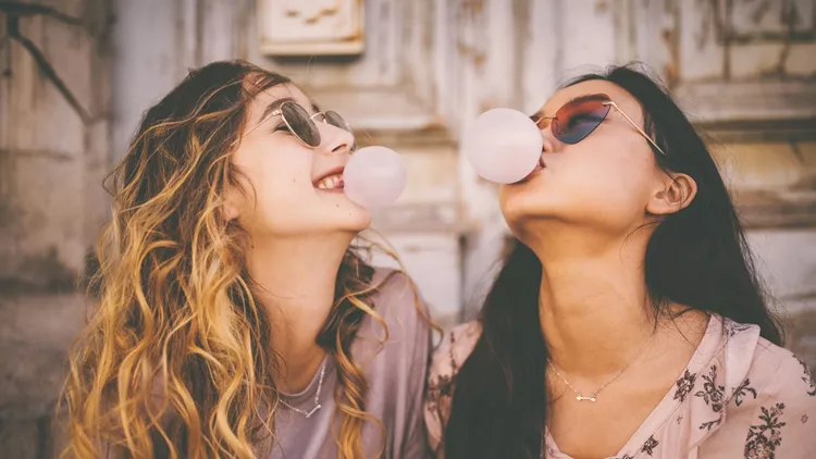 Young women blowing bubbles with bubble gum in urban setting