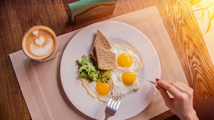 Woman eating fried eggs with toasts and coffee