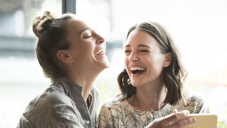 Woman holding mobile phone with freind, laughing