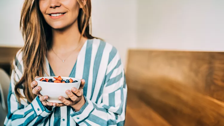 Crop woman close up eating oat and fruits bowl for breakfast