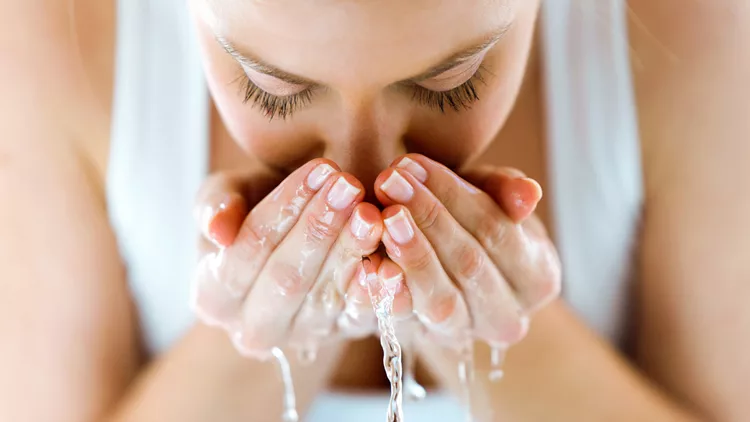 Beautiful young woman washing her face splashing water in a home bathroom.