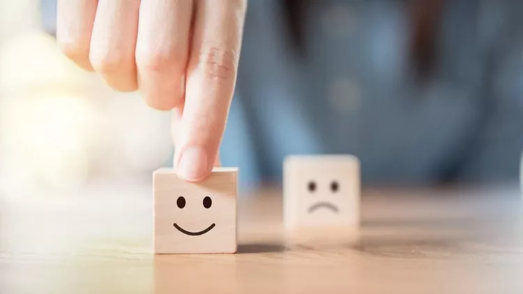 Close up hand choose smiley face and blurred sad face icon on wood cube