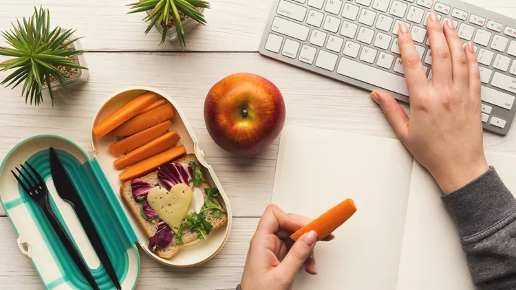 Woman eating healthy dinner from lunch box at her working table