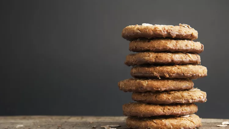 Oatmeal cookies or biscuits with oats, nuts, eggs and flour on brown dark woodenboard with black background, side view.