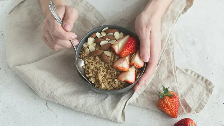 Healthy breakfast. Grey ceramic bowl with granola, strawberry and nuts in woman's hands. Diet and vegetarian food concept