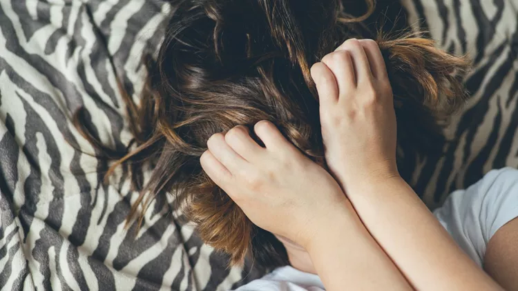 Woman lies on a bed with hands across her face.