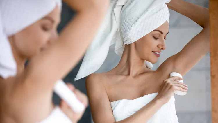 Smiling beautiful woman applying antiperspirant to armpit in bathroom