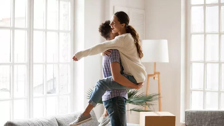 Excited couple celebrating moving day, man lifting embracing happy woman
