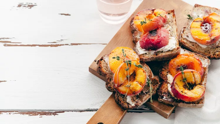 Summer snack: sandwiches with grilled peaches, cream cheese, thyme and pecan with a glass of chilled rose wine on distressed white wooden background