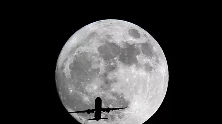 An airplane flies past the supermoon