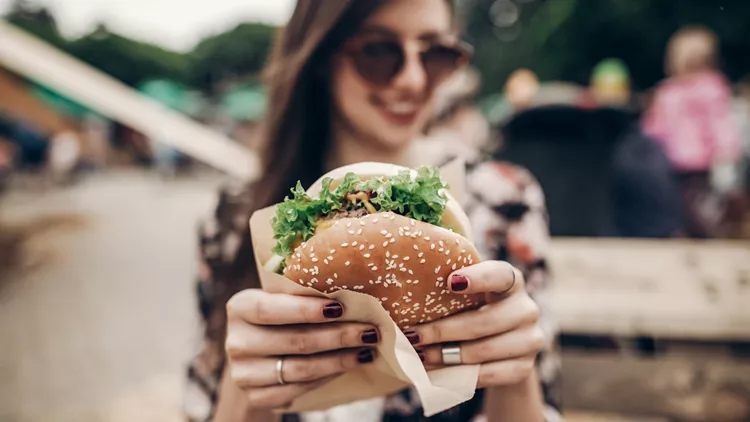 tasty burger. stylish hipster woman holding juicy hamburger in hands close up. boho girl with hamburger at street food festival. summertime. summer vacation picnic. space for text