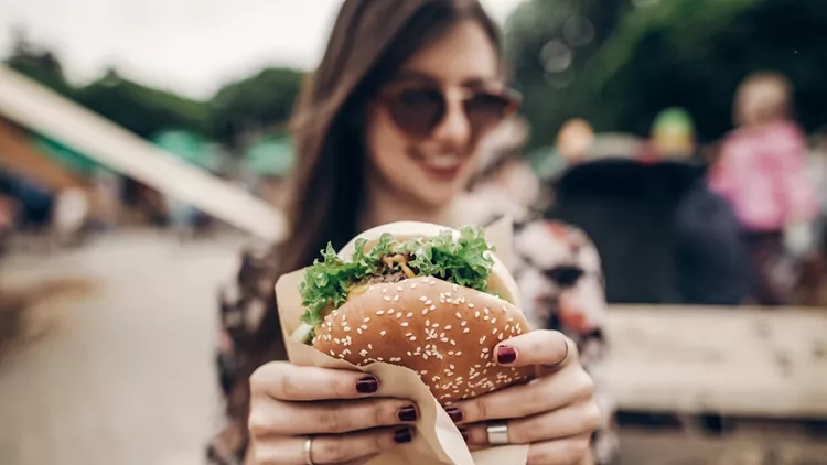 tasty burger. stylish hipster woman holding juicy hamburger in hands close up. boho girl with hamburger at street food festival. summertime. summer vacation picnic. space for text