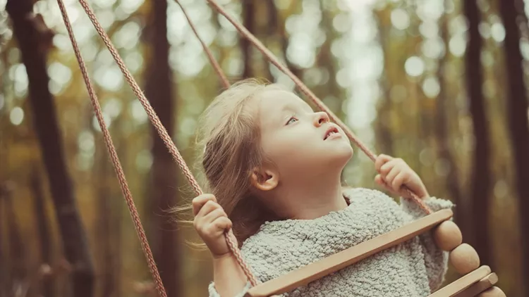 toddler girl on swing in the forest