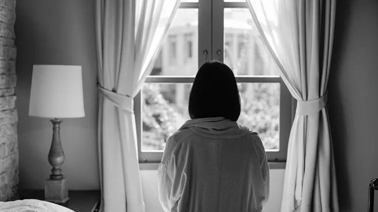 Lone woman sitting on the bed looking out at the window in the morning in black and white