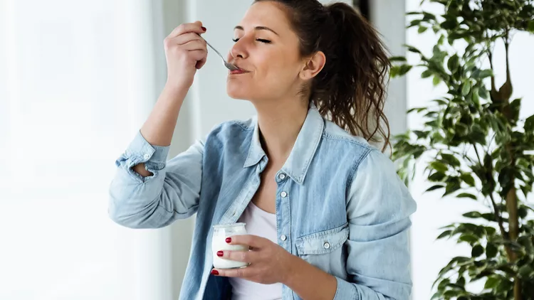 Beautiful young woman eating yogurt at home.