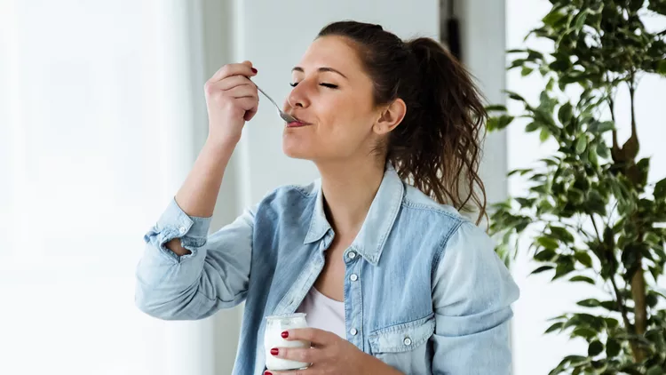 Beautiful young woman eating yogurt at home.