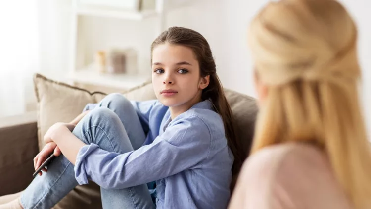 sad girl with mother sitting on sofa at home