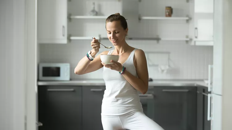 Sporty woman eating in Tree pose