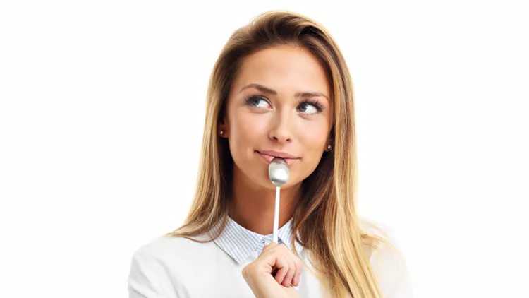 Portrait of young smiling woman with spoon in her mouth isolated on white