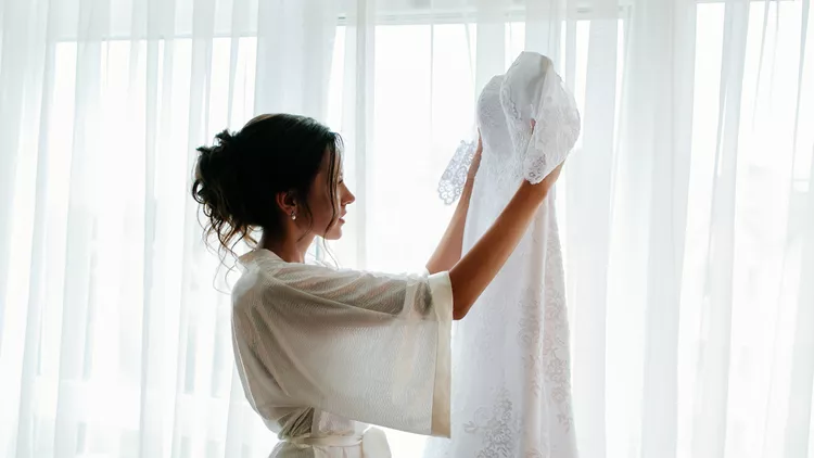 Beautiful bride holds wedding dress in hands.