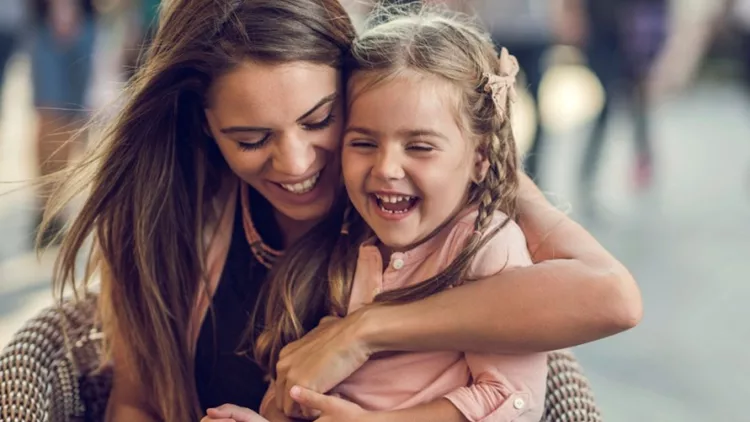 Embraced mother and daughter laughing and having fun outdoors.