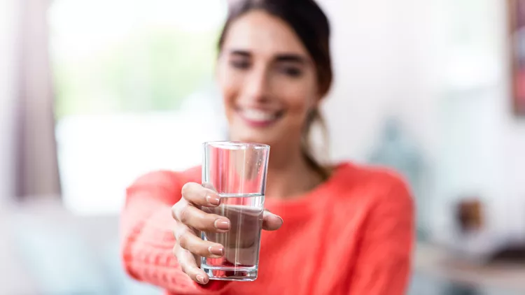 Young woman showing drinking glass with water