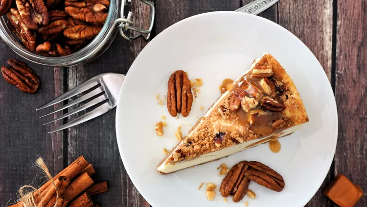 Slice of pecan caramel cheesecake, top view over wood