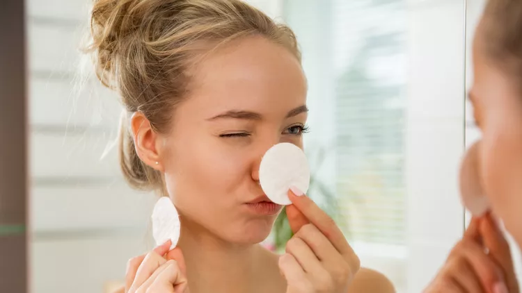 Young beautiful woman cleaning her face skin with cotton pad