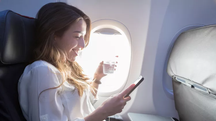 Young woman enjoys in flight beverage and wifi