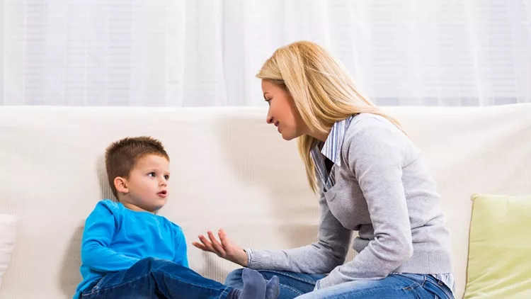Mother and son sitting on sofa and talking about something.