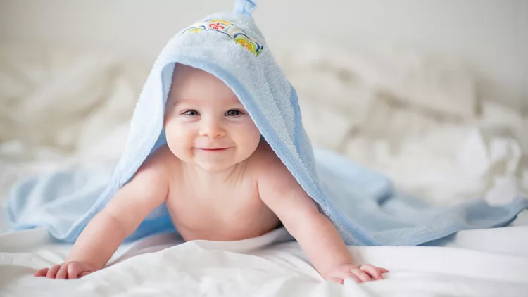 Cute little baby boy, relaxing in bed after bath, smiling happily