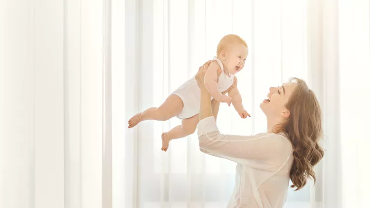 Mother with a baby in her arms plays against the window